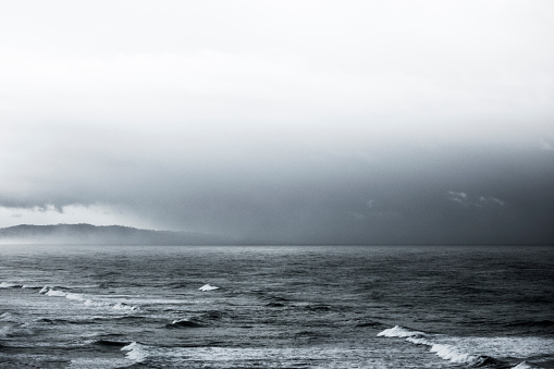 This is a black and white photo of a stormy ocean photographed from the bluff in Encinitas California at the beach on a rainy day with storm clouds rolling in and rough waves coming towards the shore