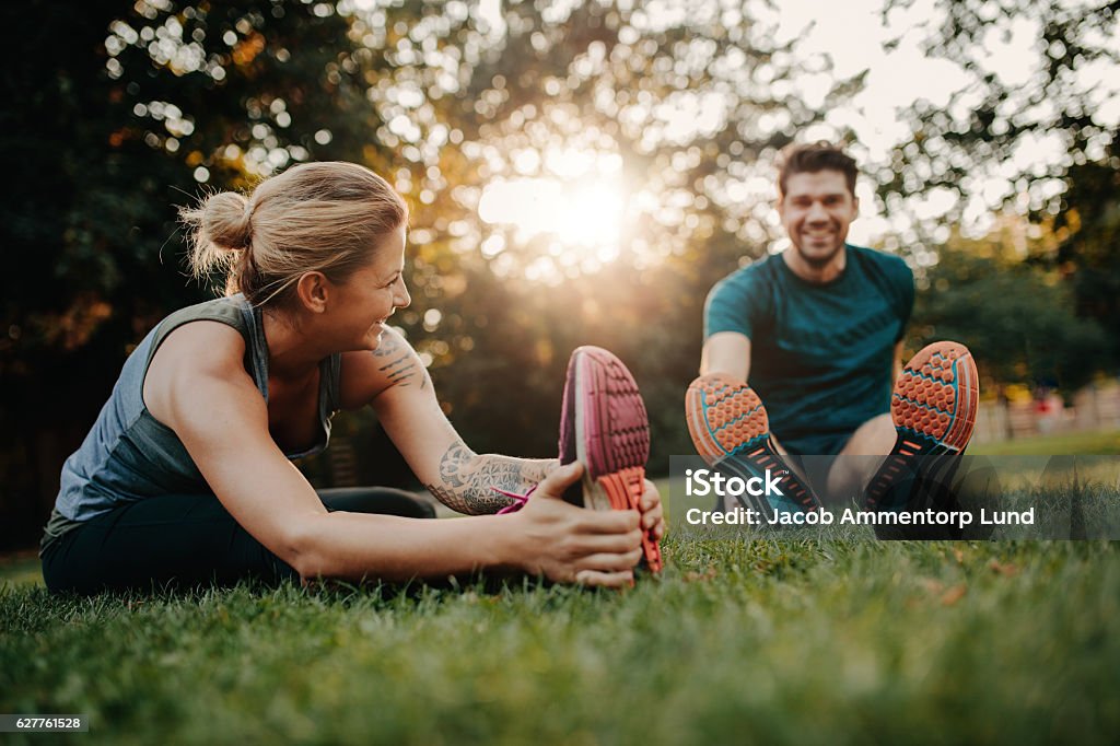Young couple doing their stretches in the park Fitness couple stretching outdoors in park. Young man and woman exercising together in morning. Exercising Stock Photo