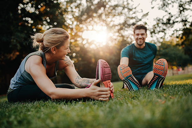 Young couple doing their stretches in the park Fitness couple stretching outdoors in park. Young man and woman exercising together in morning. warm up exercise stock pictures, royalty-free photos & images