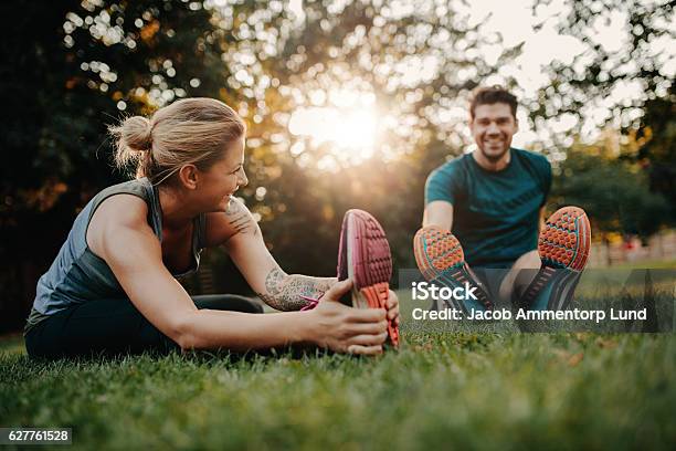 Young Couple Doing Their Stretches In The Park Stock Photo - Download Image Now - Exercising, Healthy Lifestyle, Outdoors