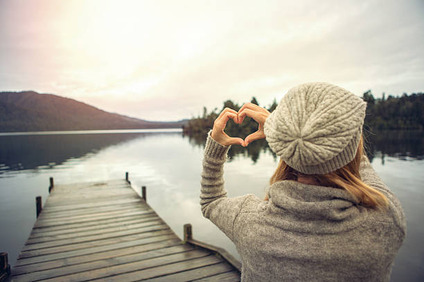 istock Young woman on lake pier, makes heart shape finger frame 627761780