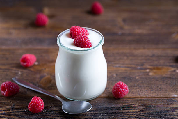 istock White yogurt with raspberries in glass bowl on rustic table. 627761976