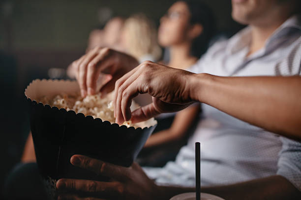 Young people eating popcorn in movie theater Close up shot of young people eating popcorn in movie theater, focus on hands. jacob ammentorp lund stock pictures, royalty-free photos & images