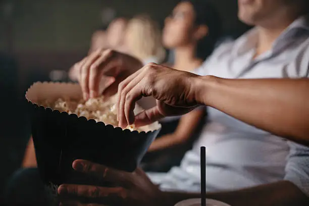 Close up shot of young people eating popcorn in movie theater, focus on hands.