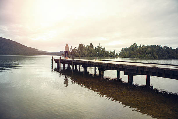 istock Lone woman standing on lake pier watching spectacular landscape 627770300