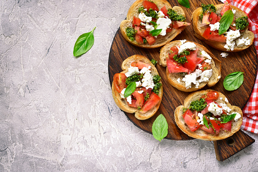 Italian bruschetta with tomatoes,feta and basil pesto on a cutting board on a. grey concrete or stone background.Top view.