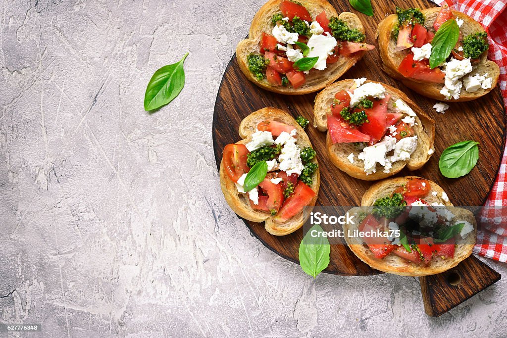 Italian bruschetta with tomatoes,feta and basil pesto. Italian bruschetta with tomatoes,feta and basil pesto on a cutting board on a. grey concrete or stone background.Top view. Pesto Sauce Stock Photo