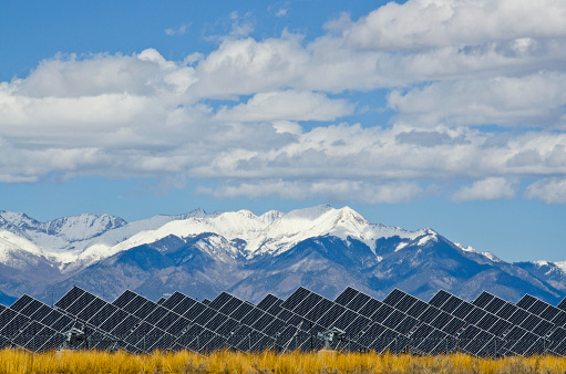 A series of large solar panels forms a symmetrical line at a power plant in the San Luis Valley of central Colorado.  The installation must be one of the most scenic in the United States, as it backs up to the snow capped Sangre de Cristo Mountains.  These panels utilize a tracking system to follow the sun, collecting its energy and using photovoltaic cells to transform the sunlight into electricity.