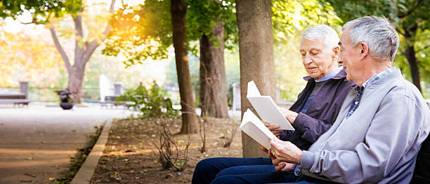 coppia gay senior maschile che si diverte a leggere libri nel panorama del parco - men reading outdoors book foto e immagini stock