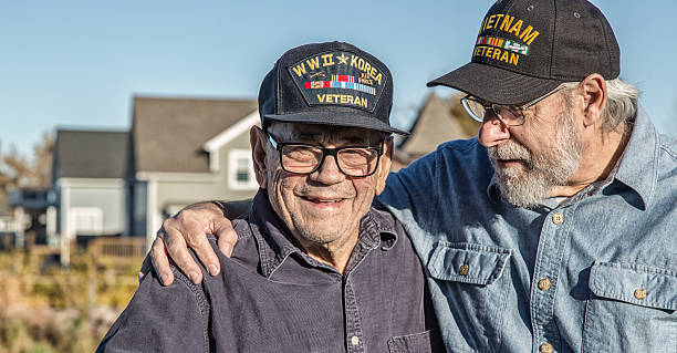 Two Generation Family USA Military War Veteran Senior Men Two generations of real person senior adult men USA military veterans. On the left, a 93 year old United States Army World War II and Korean Conflict US Air Force military veteran is smiling at the camera while his son-in-law on the right - a 65 year old US Navy sailor Vietnam War military veteran - is teasing him - trying to distract him by telling jokes during the photo shoot. They are both wearing generic souvenir shop military veteran commemorative baseball style caps. us sailor stock pictures, royalty-free photos & images