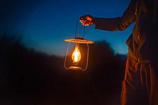 hand holds a large lamp in the dark. ancient lantern with a candle illuminates the way on a night