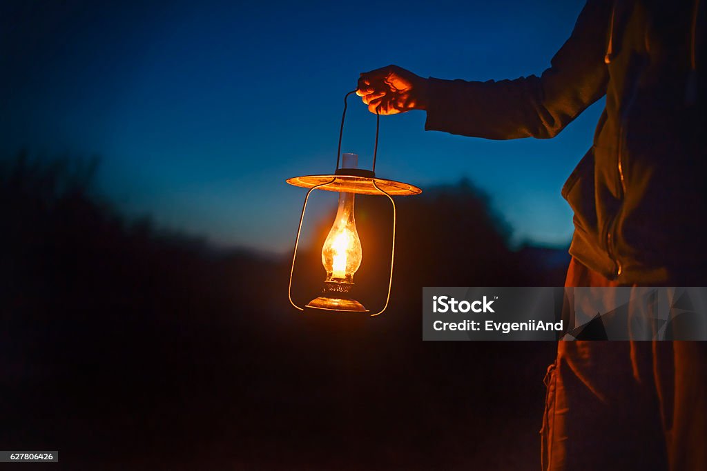 man holding the old lamp with a candle outdoors hand holds a large lamp in the dark. ancient lantern with a candle illuminates the way on a night Lantern Stock Photo