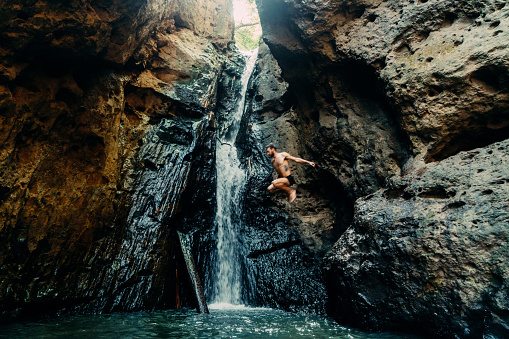 Young Caucasian man jumping from rock  into the tropical waterfall in Thailand 