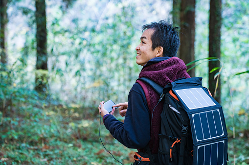 Man using solar cells strapped to his backpack to power his smartphone in the forest
