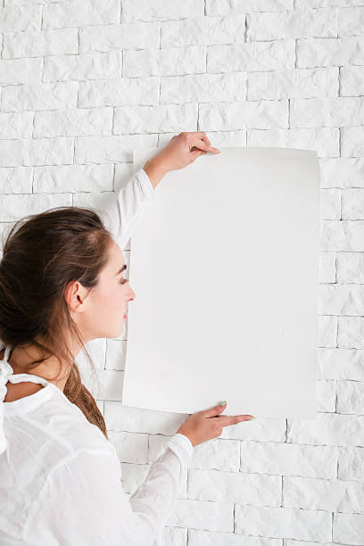istock Woman holding empty whatman at wall mockup 627815684