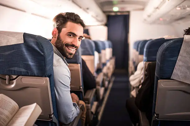 Happy man traveling by plane and turning towards the camera while looking at it.