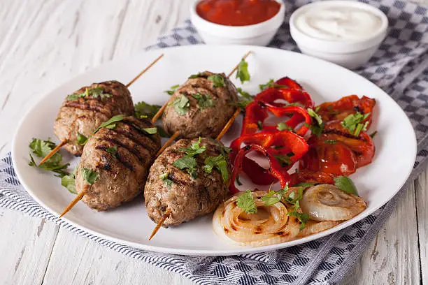 Tasty kofta kebab with grilled vegetables on a plate and sauce close-up on the table. horizontal
