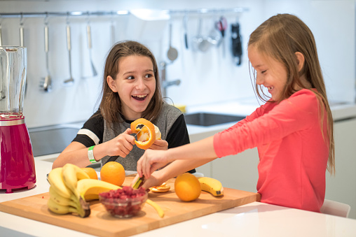Two little girls having fun in the kitchen with fresh fruit