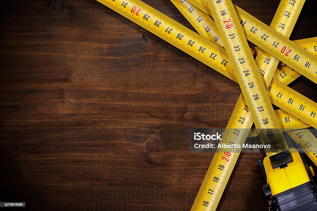 Tape Measures on Brown Wooden Background Group of tape measures on a brown wooden background (work table) with dark shadows and copy space Tape Measure Stock Photo