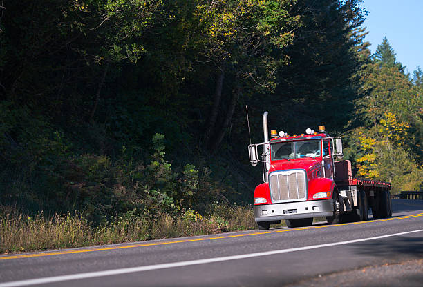 istock Red semi truck with flat bed trailer on forest road 627842066