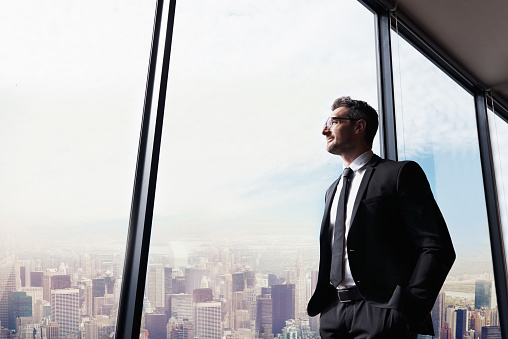 Shot of a handsome mature man looking out from a large window in the office