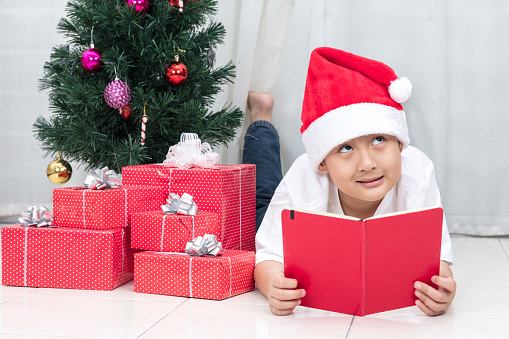 Happy Asian Chinese little boy reading book beside Christmas presents in the living room at home.