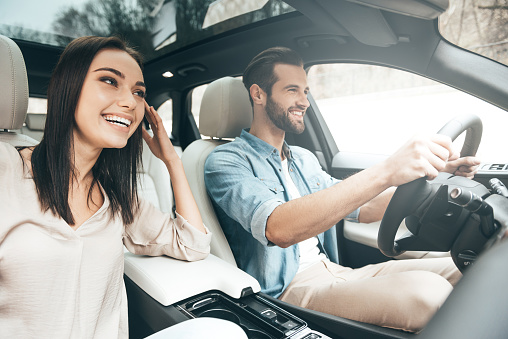 Beautiful young couple sitting on the front passenger seats and smiling while handsome man driving a car