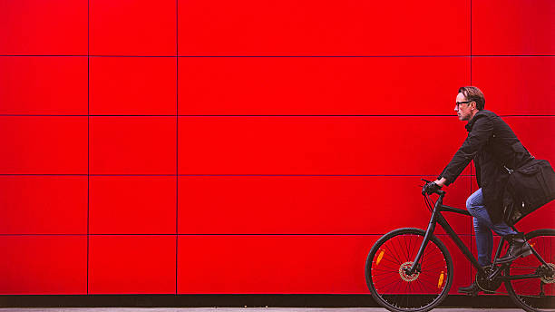 homem bonito andando de bicicleta ao lado da parede vermelha - copy space black white caucasian - fotografias e filmes do acervo