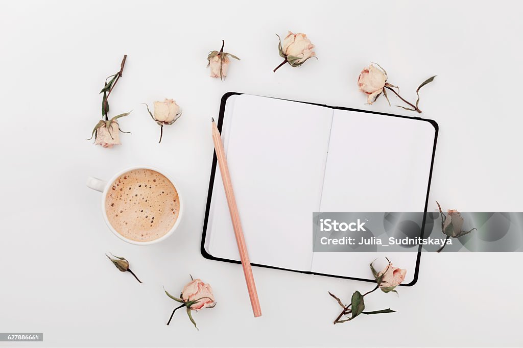 Coffee, empty notebook, dry roses flowers. Cozy Breakfast. Flat lay. Morning Cup of coffee, empty notebook and dry roses flowers on white table from above. Cozy Breakfast. Flat lay style. Note Pad Stock Photo