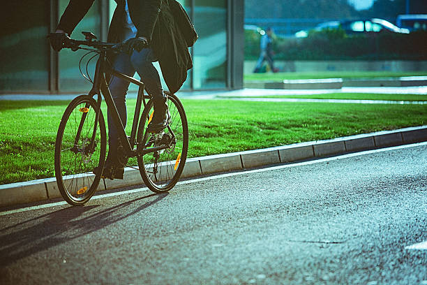 Handsome man, on the way to work, riding bicycle beside the modern office building. The man is casually dressed and wears eyeglasses and carries black briefcase hung on shoulder. Blurred motion, unrecognizable person, copy space has been left.