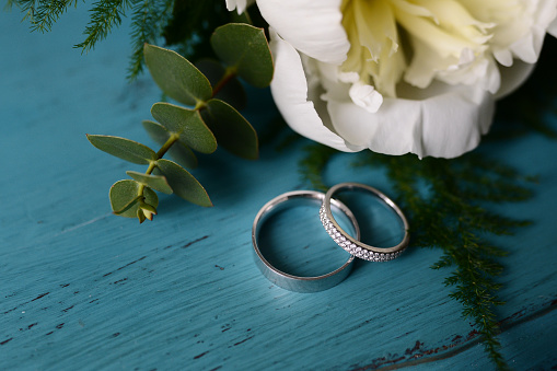 wedding rings on turquoise table with peony flower 