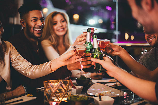 Here's to the New Year! Group of friends clinking glasses while enjoying an evening meal in a restaurant on New Years Eve. pub bar stock pictures, royalty-free photos & images