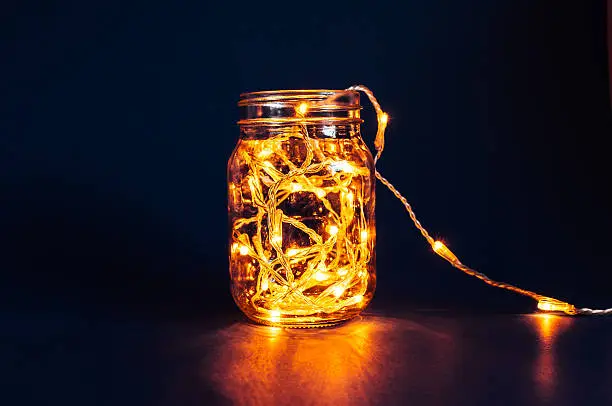 Christmas fairy lights in a mason jar, glowing in the dark, on a blue background.