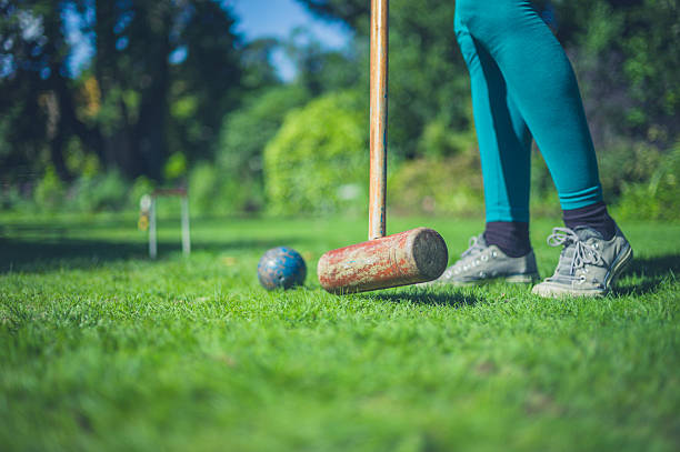 A young woman is playing croquet on a lawn