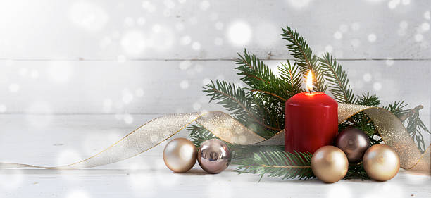 Red burning candle with christmas decoration on white wood Red burning candle with christmas decoration, fir tree, baubles and golden ribbon, in front of a white  wooden wall with bokeh lights and generous copy space, panorama, selective focus, narrow depth of field christmas decore candle stock pictures, royalty-free photos & images
