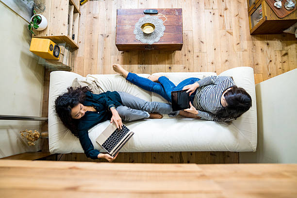 Mother and daughter laying on the sofa using smart devices stock photo