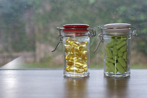 Two transparent glass bottles of dietary supplements (fish oil oyster-shell calcium) and on a windowsill, against a dirty window