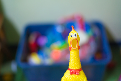 Toy rubber shriek yellow chicken on blur toy background in messy room, kid room, shellow DOF