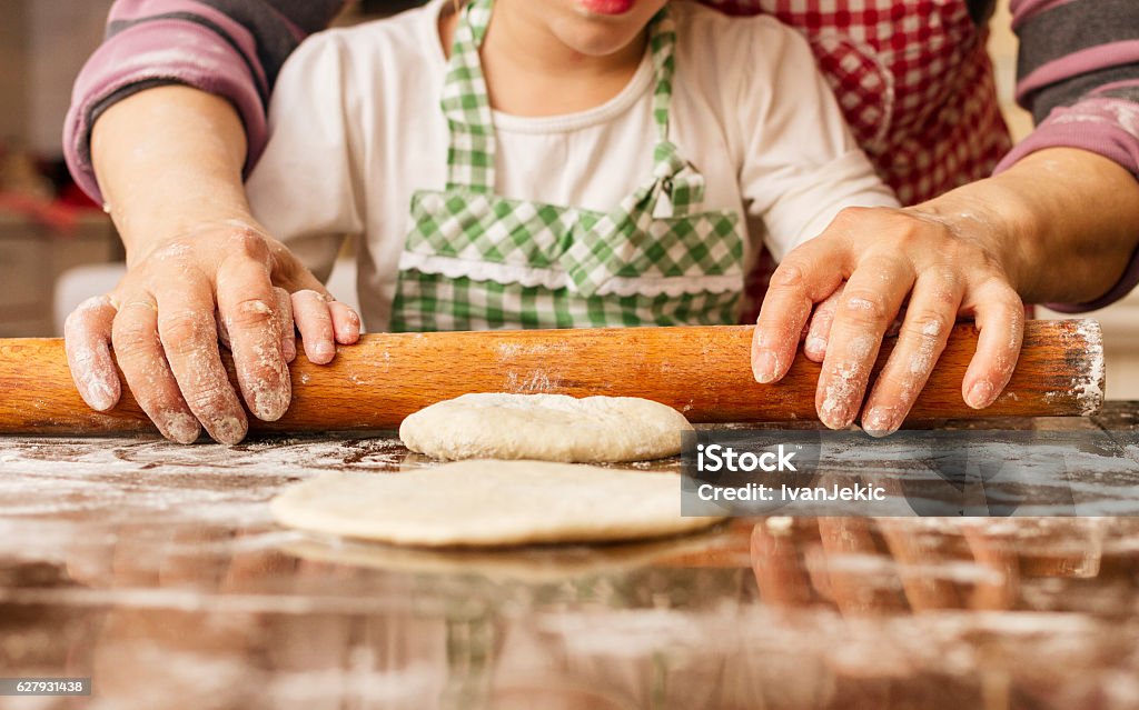 Grandma and granddaughter stretching dough Little granddaughter is stretching the dough with her grandma. Focus is on the action and hands covered with flour. Genuine family. Grandmother Stock Photo