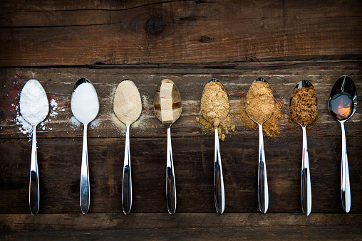 Different Kinds of Sugar in the Spoons, such as coconut sugar, pure cane sugar, icing sugar, agave syrup, dark brown soft sugar, golden caster sugar, demerara cubes