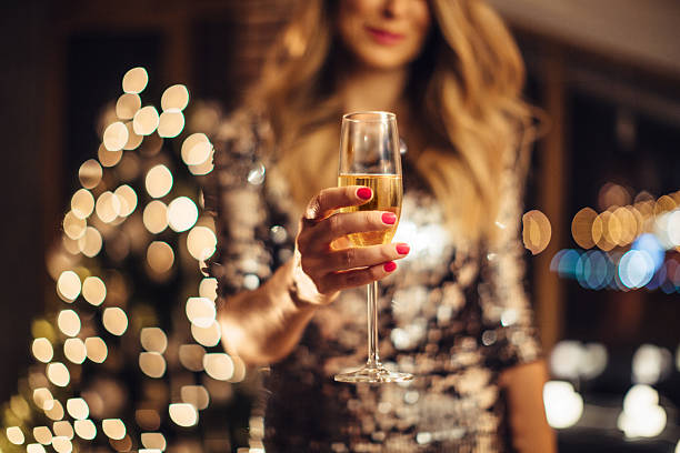 Happy New Year Close up of woman's heands holding glass of champagne. Woman wearing sparkly elegant dress. Evening or night with Christmas tree in background. campania photos stock pictures, royalty-free photos & images