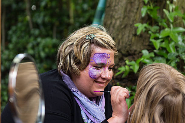 Woman with painted face painting faces at event stock photo