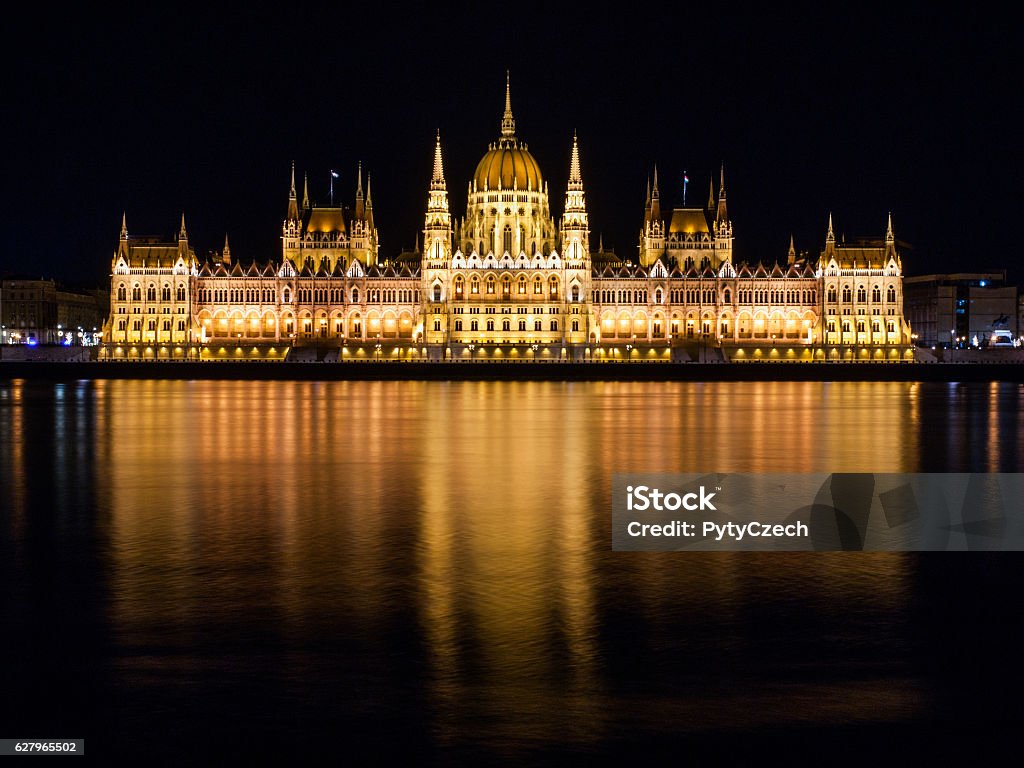 Illuminated historical building of Hungarian Parliament on Danube River Embankment Night view of illuminated historical building of Hungarian Parliament, aka Orszaghaz, with typical symmetrical architecture and central dome on Danube River embankment in Budapest, Hungary, Europe. It is notable landmark and seat of the National Assembly of Hungary. Budapest Stock Photo