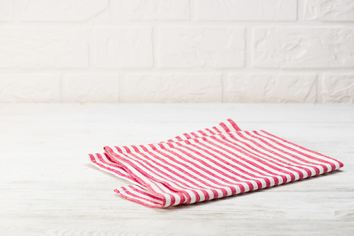 Red napkin isolated on white wooden table. Copy space. White brick wall background. Front view.