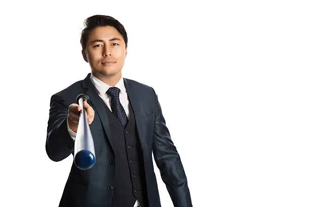 Handsome staring businessman in a suit with vest and tie, holding a baseball bat, staring at camera. White background.