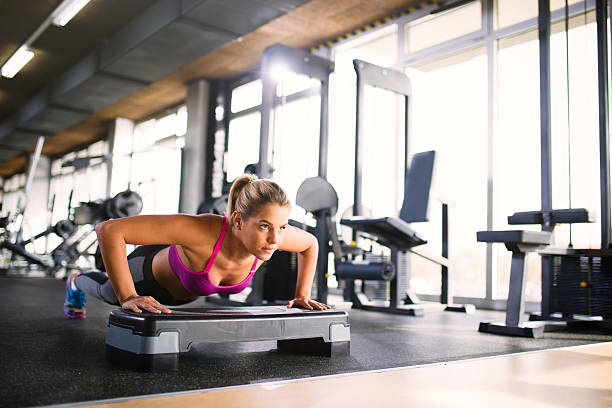 Athletic women doing push-ups on step aerobics equipment  at gym.