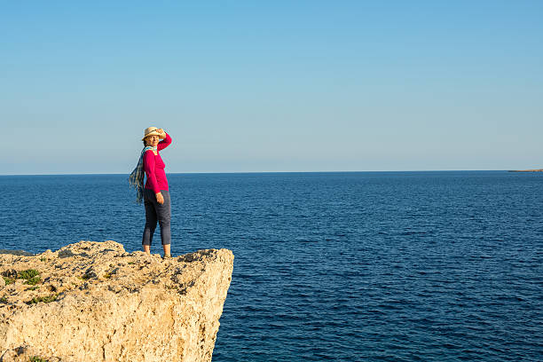 istock Woman in a straw hat standing on the rocky shore 627977554