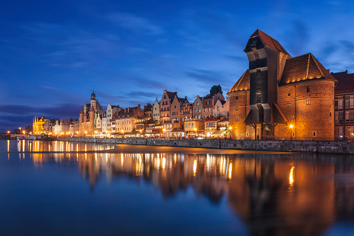The old town of Gdansk by the Motlawa river in the evening. On the right is a historical wooden crane, a landmark in the city.