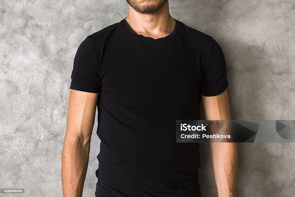 Man in black shirt closeup Closeup of young man's body in empty black t-shirt on textured concrete wall background. Mock up Adult Stock Photo