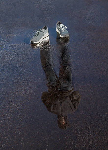 Senior caucasian man reflected in wet pavement, with shoes on pavement